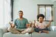 © eggeeggjiew - Cheerful African American father and Cute boy smiling relaxed with closed eyes sitting on couch meditating together, Black Family practicing yoga at home