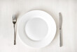 © zenobillis - White clean plate and stainless knife and fork on light wooden table. Served cutlery. Top view