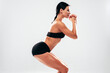 © halayalex - Fitness confident woman in black sports clothing. Sexy young beautiful model with perfect body. Female isolated in studio. Stretching out before training.Making squats on grey background