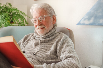 Wall Mural - Portrait of beautiful relaxed senior man sitting at home on armchair reading a book - old generation and retirement concept