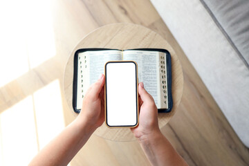 Woman hand hold and touch screen smart phone,cellphone in church over blurred bible holy and age book.