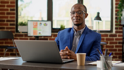 Wall Mural - portrait of african american worker sitting at office desk, using laptop to work on executive projec