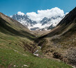Georgia, Caucasus Mountains, Juta valley - river, green hill, blue sky, mountain from stones and snowy peak Chaukhebi in summer - pano