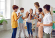 © Studio Romantic - Children's education. Funny schoolchildren and their positive female teacher play fun games in creative lesson. Elementary school students laugh loudly and clap their hands together in classroom.