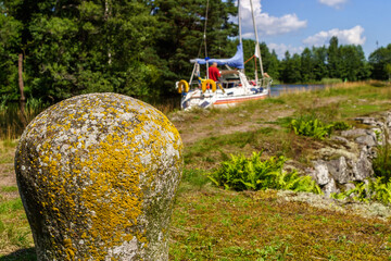 Poster - Old stone bollar at a canal with a sailboat