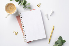 Business Concept. Top View Photo Of Workspace Open Notepad Eucalyptus Cup Of Coffee Gold Pen Binder Clips And Wireless Earbuds On Isolated White Background With Blank Space,