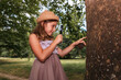 © _KUBE_ - Children's education and curiosity. Portrait of caucasian little girl in a straw hat looks at the tree bark through a magnifier. Side view.The concept of scouting and childhood