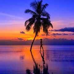 Sunset on Maldives island, luxury water villas resort, pool and palm tree. Beautiful sky and beach with palms landscape. Summer vacation and travel concept. Woman silhouette on the sunset background