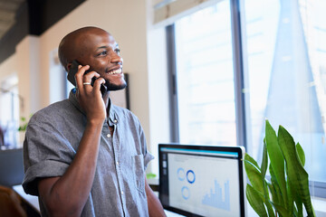 Wall Mural - A Black businessman answers the phone standing smiling in trendy office