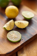 Wall Mural - Close-up of fresh green and yellow  organic lemon (Citrus limon) and slices and pieces of lemon on a wooden cutting board with green leaf.