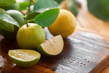 Wall Mural - Close-up of fresh green and yellow  organic lemon (Citrus limon) and slices and pieces of lemon on a wooden cutting board with green leaf.