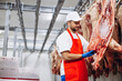 © Petro - Man butcher standing by hanging fresh pork at the freezer
