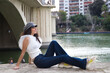 young, beautiful woman with dark, curly hair and an upturned nose is wearing a cap and sitting by a river. The woman is posing for photos. Concept expressions. smile, sad, thinking, enjoying, living.