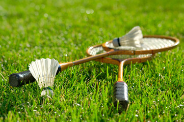 Playing badminton on a green sports lawn. On the short-cropped grass lies a set of rackets and two shuttlecocks.