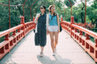 full length with front view happy asian visitor besties are appreciating the design while walking together on an Japanese red bridge during sunny summertime.