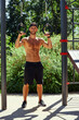 © Georgii - Shirtless man doing loop exercises outdoors in summer park.