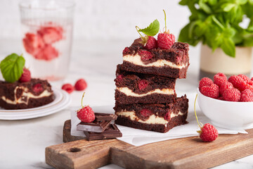 Brownie cake bars with cheesecake layer, dark chocolate and raspberries. Delicious summer homemade dessert. 