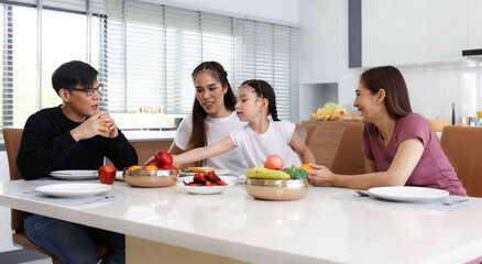 A large, happy Asian family spends their time dining at the tables inside the house. Little daughter having fun chatting