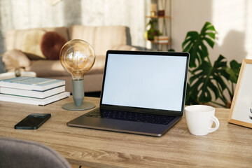 Wall Mural - Blank screen laptop, cell phone and a cup on wooden table. Cozy lofty office with house plants full of natural sunlight. Close up, copy space, background.