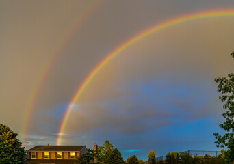 Double rainbow after the rain over the roof of rural house and trees in Aurora, Colorado