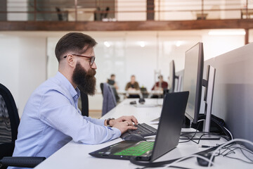 Senior computer programmer developer working in IT office, sitting at desk and coding, working on a project in software development company or startup.