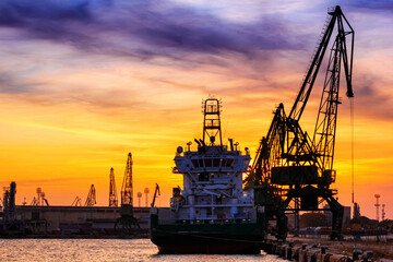  Silhouettes of harbor cranes and cargo ships in the seaport of Varna at sunset, on the Black Sea coast of Bulgaria