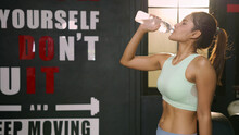 Asian Athlete Woman In Sportswear Is Holding Bottle And Drinking Water Before Cardio Workout In Fitness Gym. Sports Woman Drinking And Preparing To Do Bodyweight Training. Bodybuilding At Gym Concept