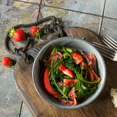 Wall Mural - a bowl of salad with jamon, arugula, tomatoes and strawberries on the table