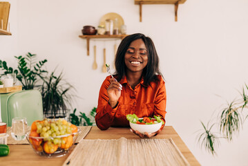 Wall Mural - Beautiful young woman eating salad in the kitchen in the morning. Healthy food. Close up. Portrait shot