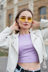 Wall Mural - Fashionable beautiful hipster street girl with stylish yellow sunglasses and purple T-shirt with leather jacket in the city