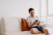 Happy asian man using smartphone in his living room in a casual day.
