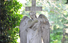 An Old, Weathered Sandstone Sculpture Of A Grieving Angel On A Cemetery In Berlin Germany.