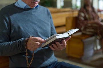 Wall Mural - Hands of aged man holding open Bible and wooden rosary beads while reading verses from Gospel or some other book during sermon