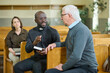 © pressmaster - African American priest in black casualwear and clerical collar having discussion with senior male parishioner after church service