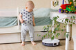 Cute baby boy toddler watching with interest for white robotic vacuum cleaner.