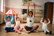 © Drazen - Happy black preschool teacher and group of kids stretching during exercise class.