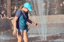 The Child Is Saved From The Heat In The Fountain. Girl 10-12 Years Old Is Cooled By Water Splashes. Swim In The Fountain In Summer.
