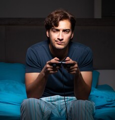 Wall Mural - Young man playing computer games at night in bed