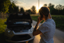 One Woman Mature Female Standing On The Road In The Evening Sunset By The Broken Vehicle Car Automobile Failed Engine Open Hood Making A Phone Call For Help Roadside Assistance Towing Service Concept
