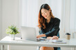 © ArLawKa - Smiling happy Asian woman relaxing using the technology of a laptop computer while sitting in a chair at a desk. creative girl working at home The concept of working and studying online learning