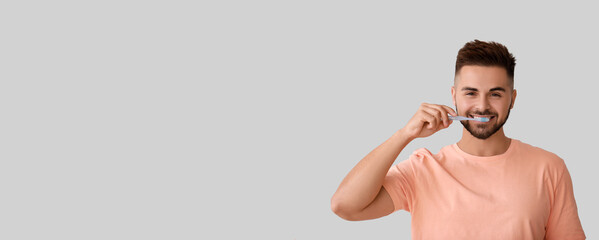 Wall Mural - Portrait of handsome young man brushing teeth on light background with space for text