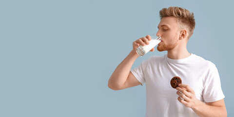 Handsome young man with tasty cookie drinking milk on color background with space for text