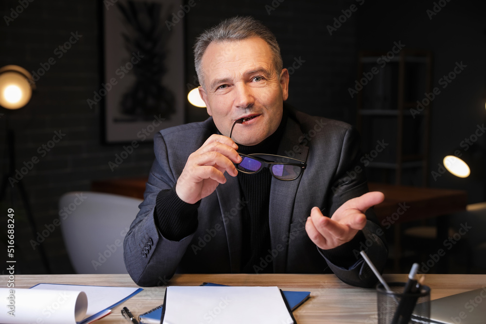 Mature businessman video chatting in office at night