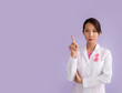 © Pixel-Shot - Female Asian oncologist with pink ribbon on lilac background. Breast cancer awareness concept