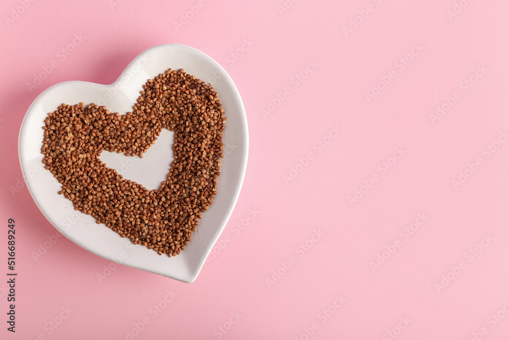 Heart shaped plate with buckwheat grains on pink background