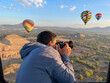 Young man photographing colorful Hot Air Balloons Flying Over Ancient Pyramid of Teotihuacan, Mexico at sunrise -sunset, over the mist