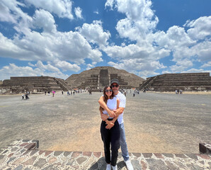 Young beautiful couple of tourists posing in front of the ruins of Teotihuacan, Mexico - The Avenue of the Dead, the pyramid of the sun and the pyramid of the moon