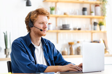 young concentrated man student in headset using laptop sitting in home, distance learning, online ed