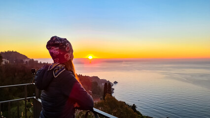 Wall Mural - Tourist woman with scenic view on beautiful landscape at sunrise at Mediterranean Ionian sea seen from the main square (Piazza IX Aprile) in Taormina, Province of Messina, Sicily, Italy, Europe, EU