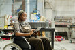 © AnnaStills - African female worker with disability using digital tablet at work while sitting in wheelchair at workshop
